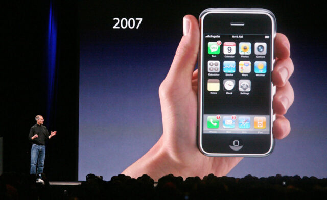 Steve Jobs on stage holding the original iPhone